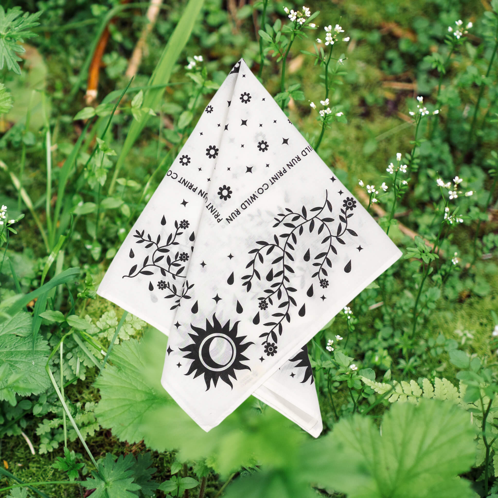 The Wild Run Print Co. botanical bandana with a black and white vines, leaves and sun print on a lush green leafy photo background