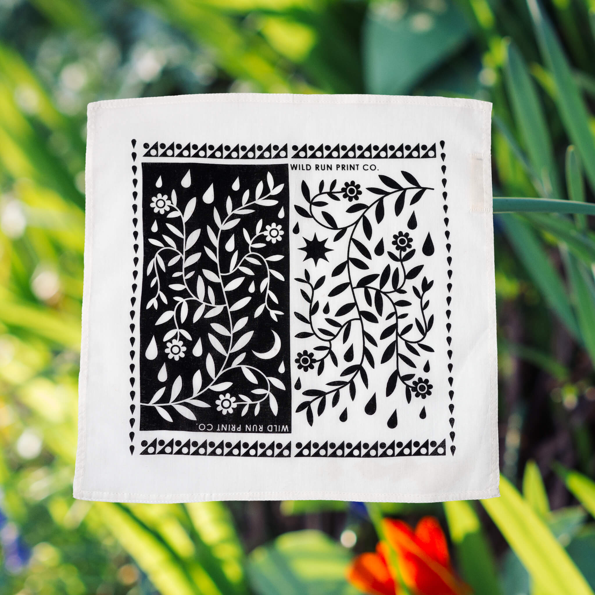 The Wild Run Print Co. raindrop hankie on an out of focus photo of spring flowers and green leaves