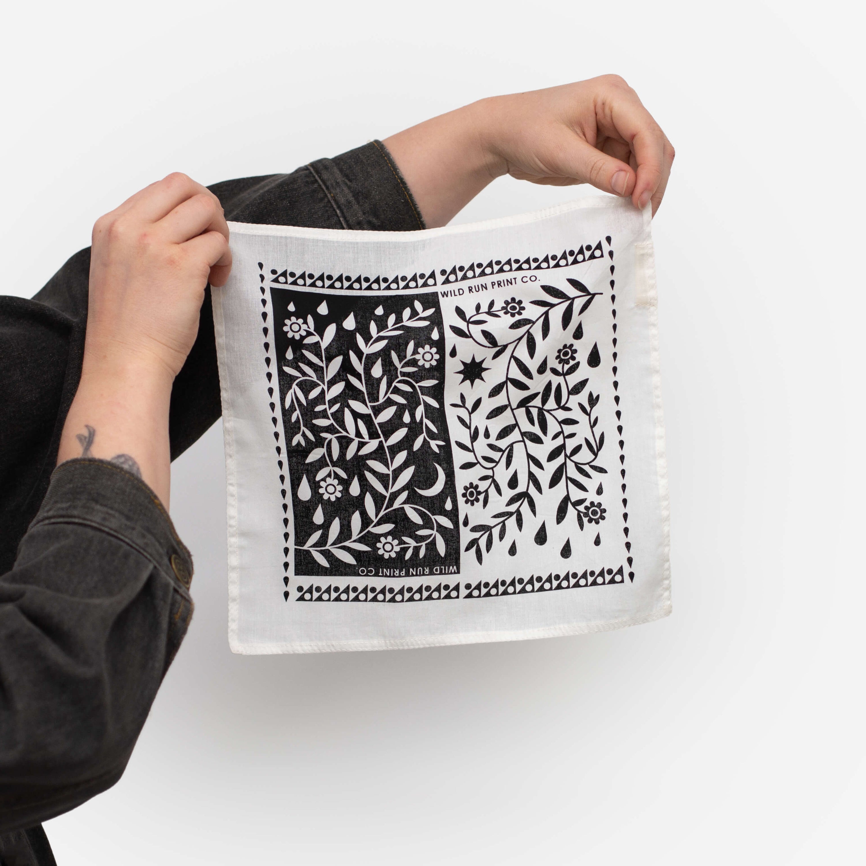A person holds up a white, organic hankie, printed with a black and white raindrop botanical design